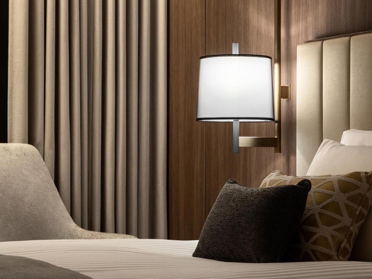 Mitsui Garden Hotel Roppongi Tokyo Premier Zewnętrze zdjęcie The photo displays a cozy hotel room setting. It features a neatly made bed with white linens and several decorative pillows. To the side, there’s a stylish bedside lamp mounted on the wall with a round white shade. Behind the lamp, there are elegant