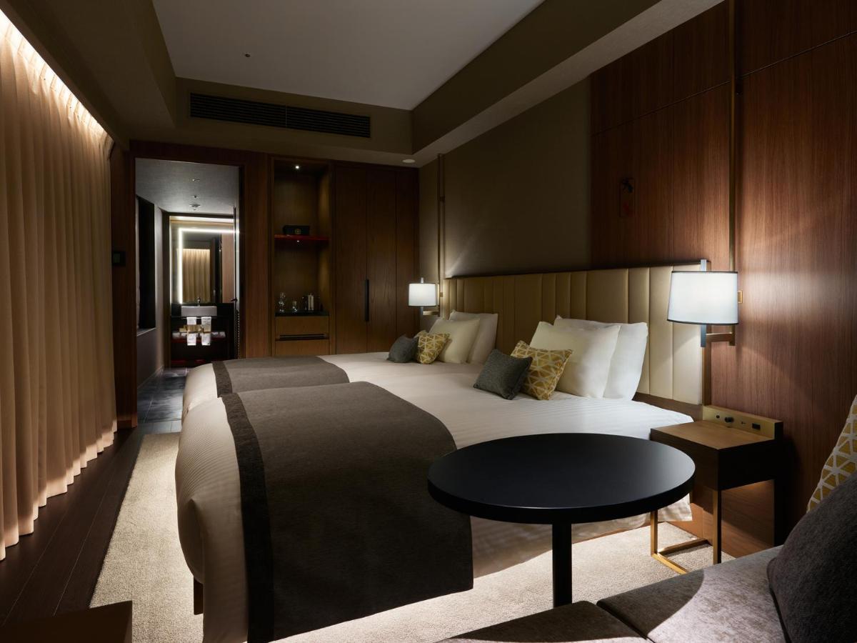 Mitsui Garden Hotel Roppongi Tokyo Premier Zewnętrze zdjęcie The photo shows a stylish hotel room featuring two beds with plush bedding and decorative pillows. The walls are made of wood, creating a warm and modern atmosphere. There are bedside lamps on each side of the beds providing soft lighting. A small ro