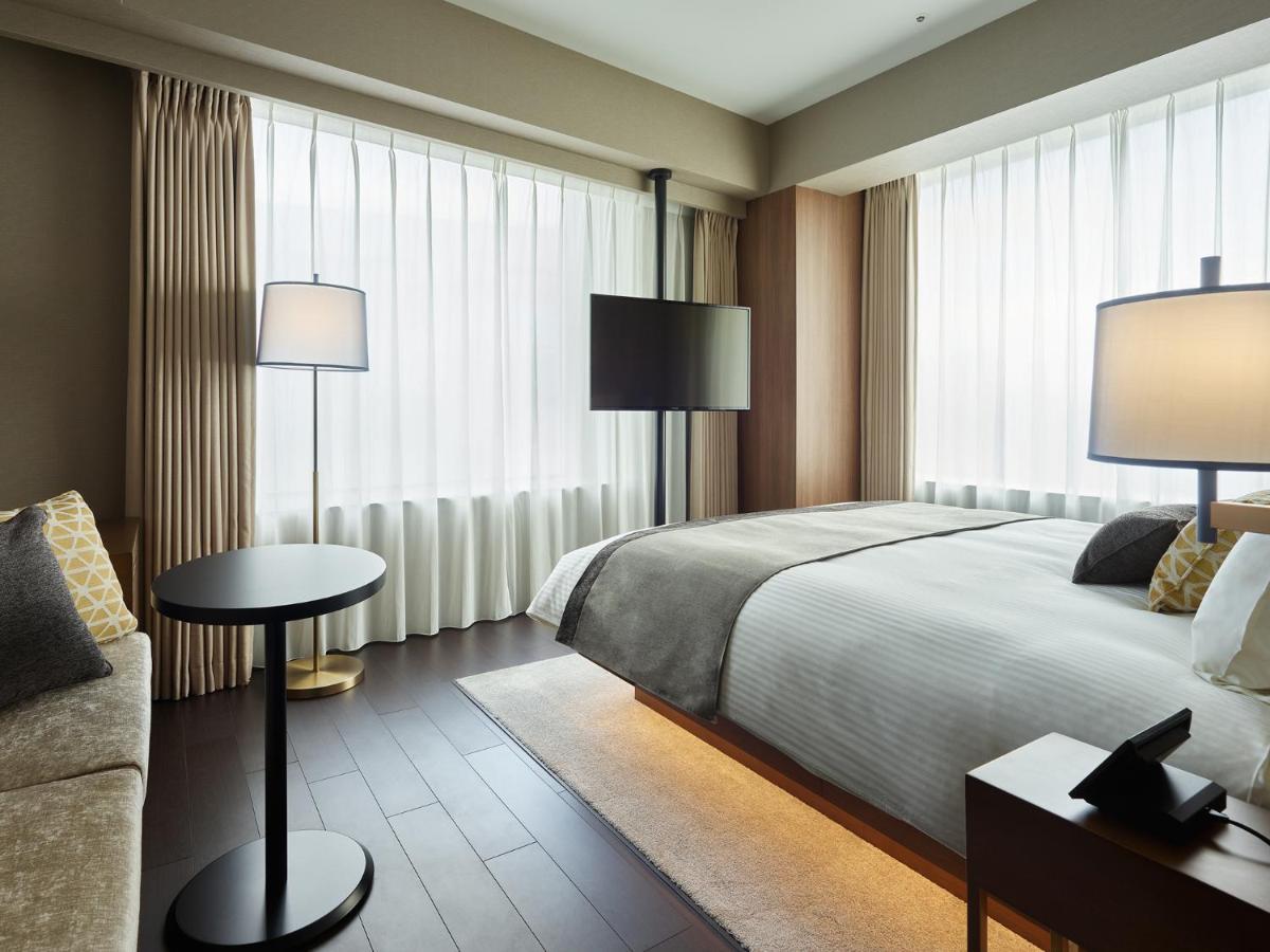Mitsui Garden Hotel Roppongi Tokyo Premier Zewnętrze zdjęcie The photo shows a modern hotel room with a contemporary design. It features a large bed with crisp white linens, sitting against a wall with floor-to-ceiling windows covered by sheer curtains, allowing natural light to filter in. To the side, there's