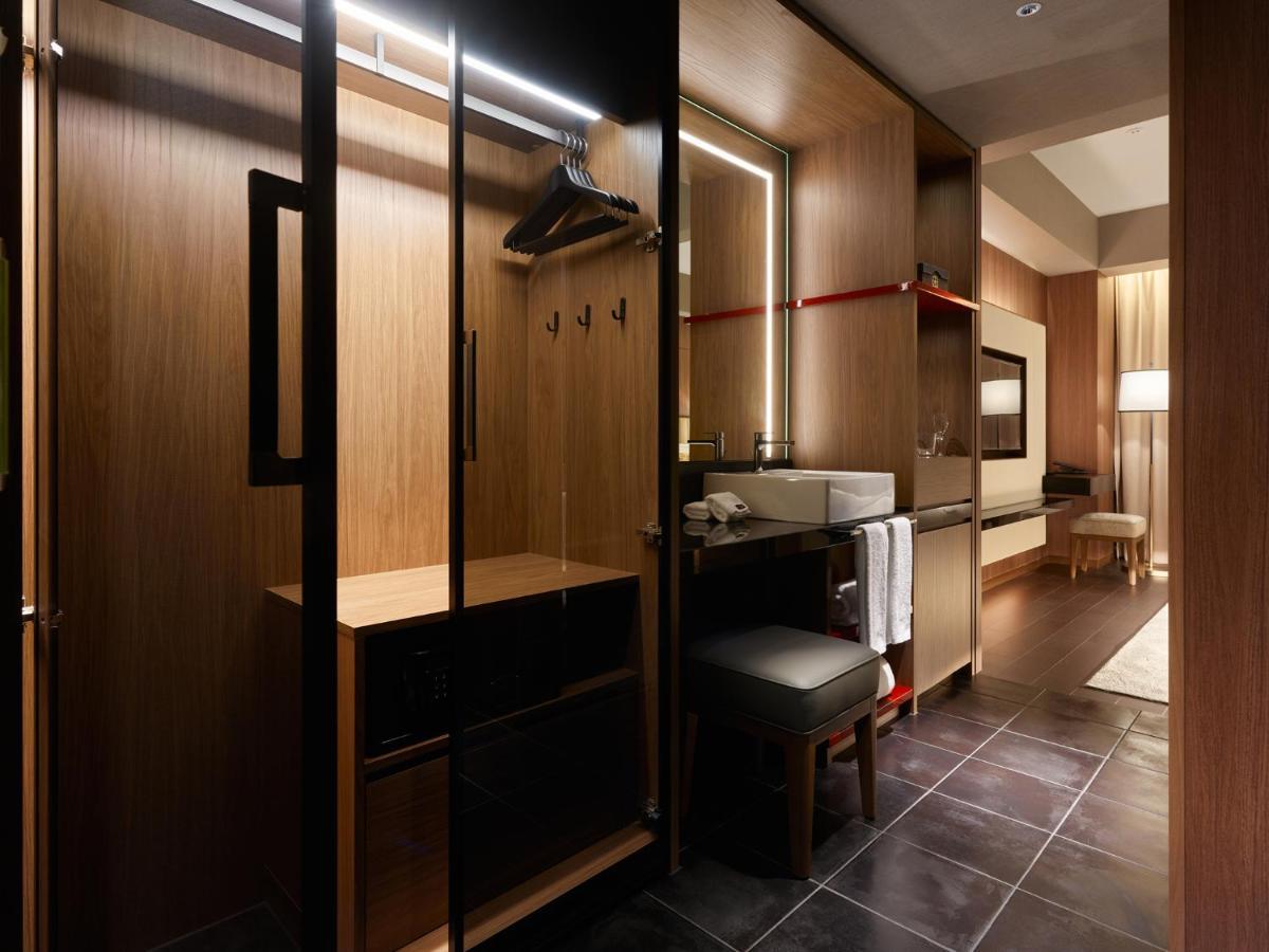 Mitsui Garden Hotel Roppongi Tokyo Premier Zewnętrze zdjęcie The photo depicts a modern and stylish hotel room's closet area. It features wooden cabinetry with a sleek finish, including mirrored doors. Inside, there are hangers for clothing and hooks mounted on the wall. A small bench or chair is positioned ne