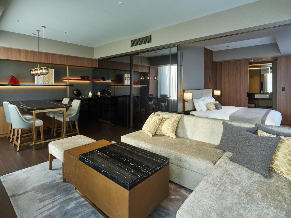 Mitsui Garden Hotel Roppongi Tokyo Premier Zewnętrze zdjęcie The image shows a modern hotel room or suite that features a contemporary design. Key elements include:

- A comfortable seating area with a light-colored sofa and a stylish coffee table.
- A dining area with a table and chairs, suggesting space for 