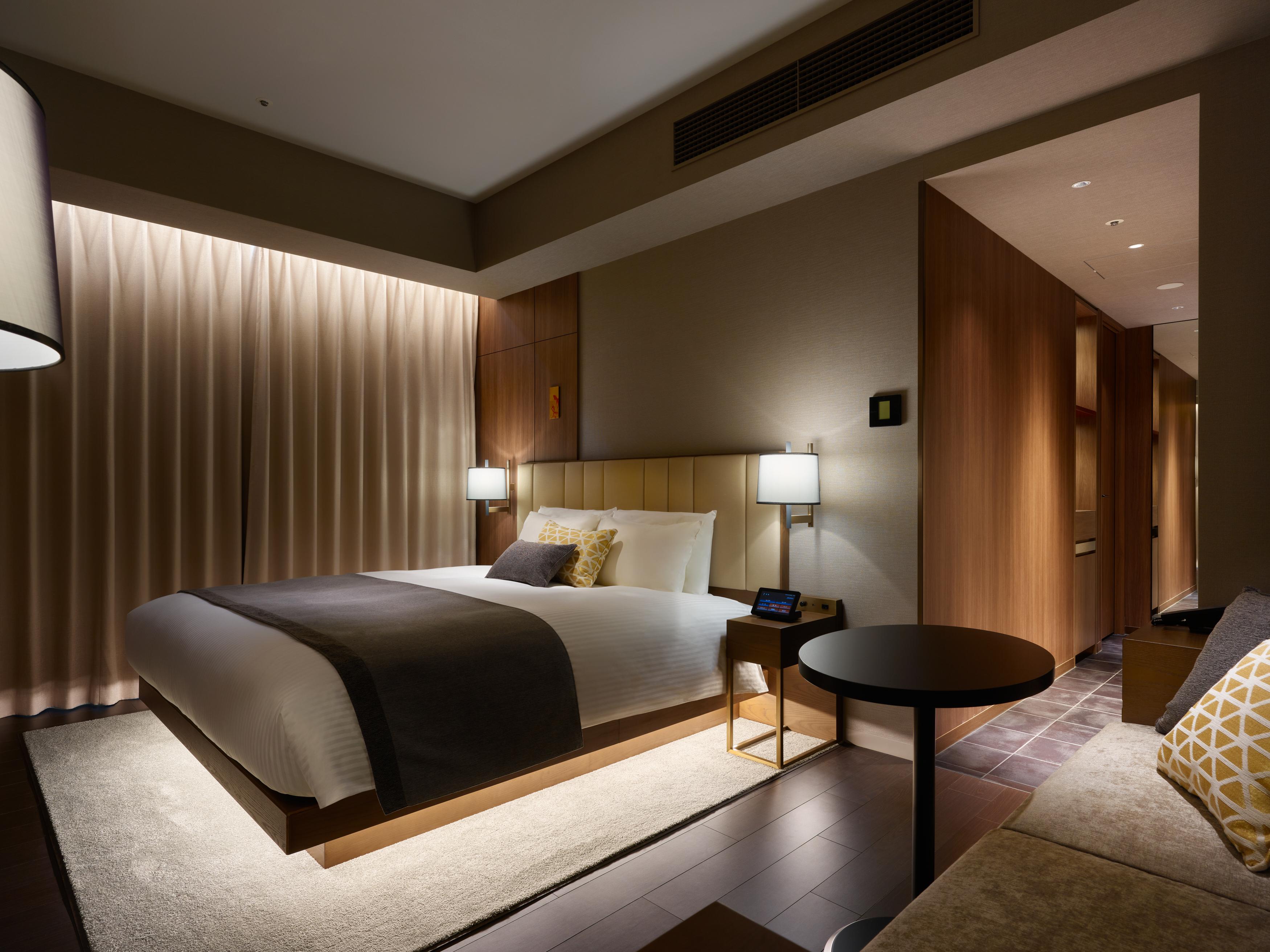 Mitsui Garden Hotel Roppongi Tokyo Premier Zewnętrze zdjęcie The photo shows a modern hotel room featuring a king-sized bed with neutral-colored bedding and accent pillows. There are two bedside lamps on either side of the bed, providing a warm glow. The walls have a wood finish, and there's a soft area rug on