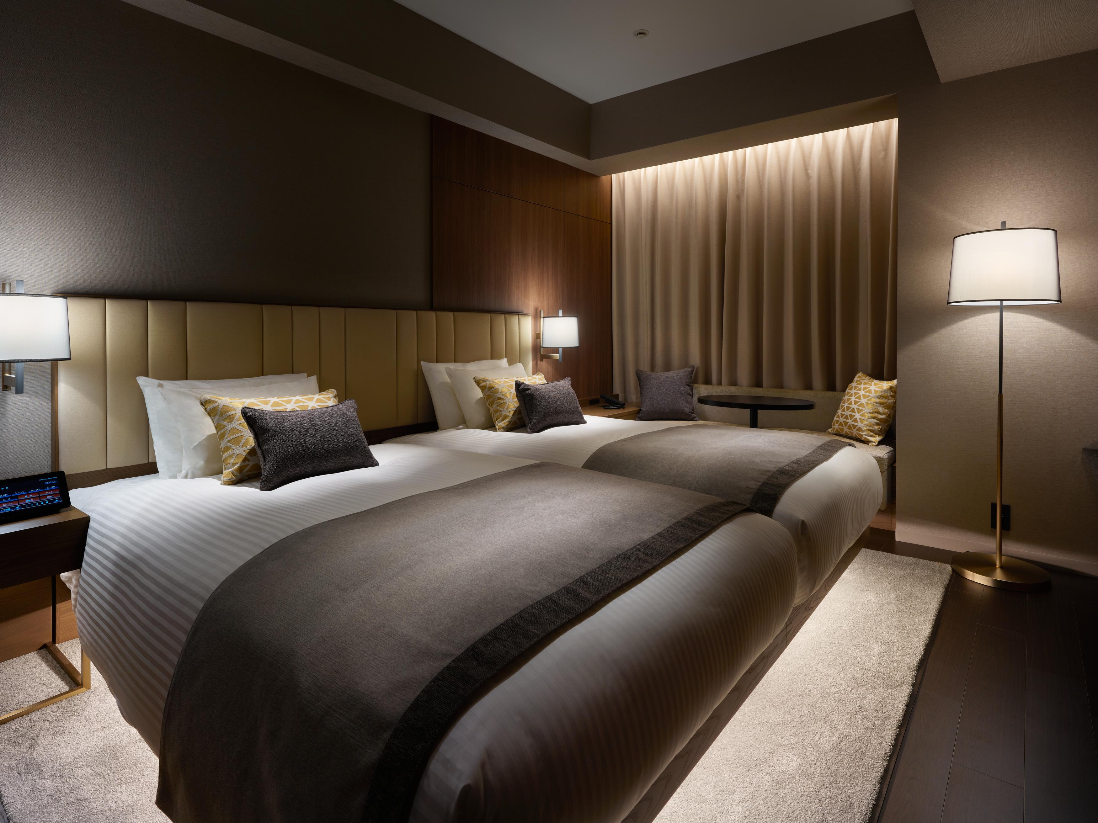 Mitsui Garden Hotel Roppongi Tokyo Premier Zewnętrze zdjęcie The photo shows a modern hotel room featuring two beds with elegant bedding in neutral colors. Each bed is adorned with decorative pillows. The room has a sophisticated ambiance with dim lighting, highlighted by table lamps on either side of the beds