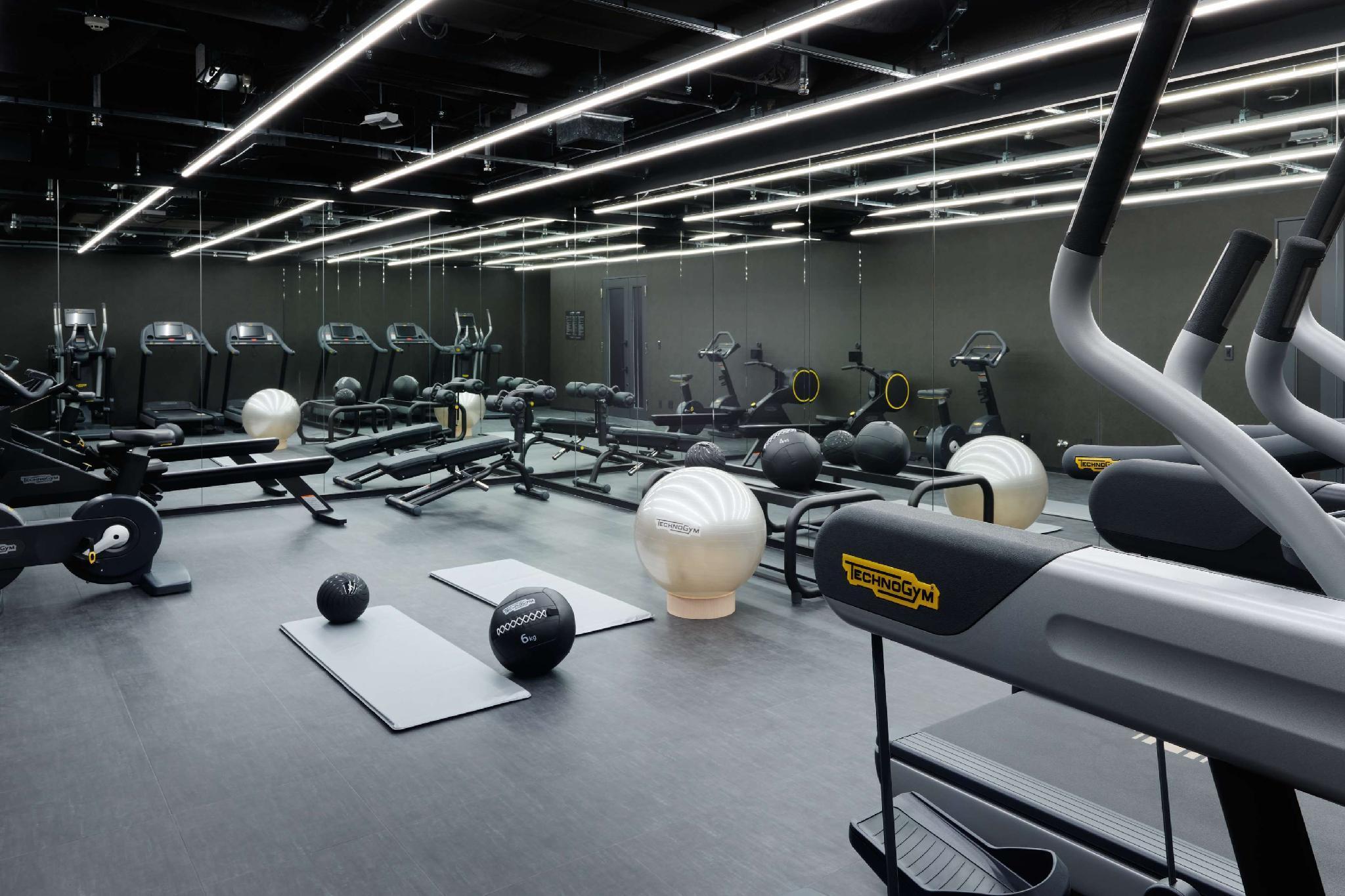 Mitsui Garden Hotel Roppongi Tokyo Premier Zewnętrze zdjęcie The photo shows a modern gym interior. The space features various exercise equipment, including cardio machines like treadmills and elliptical trainers, weight machines, and free weights. There are also exercise mats and fitness balls scattered throu