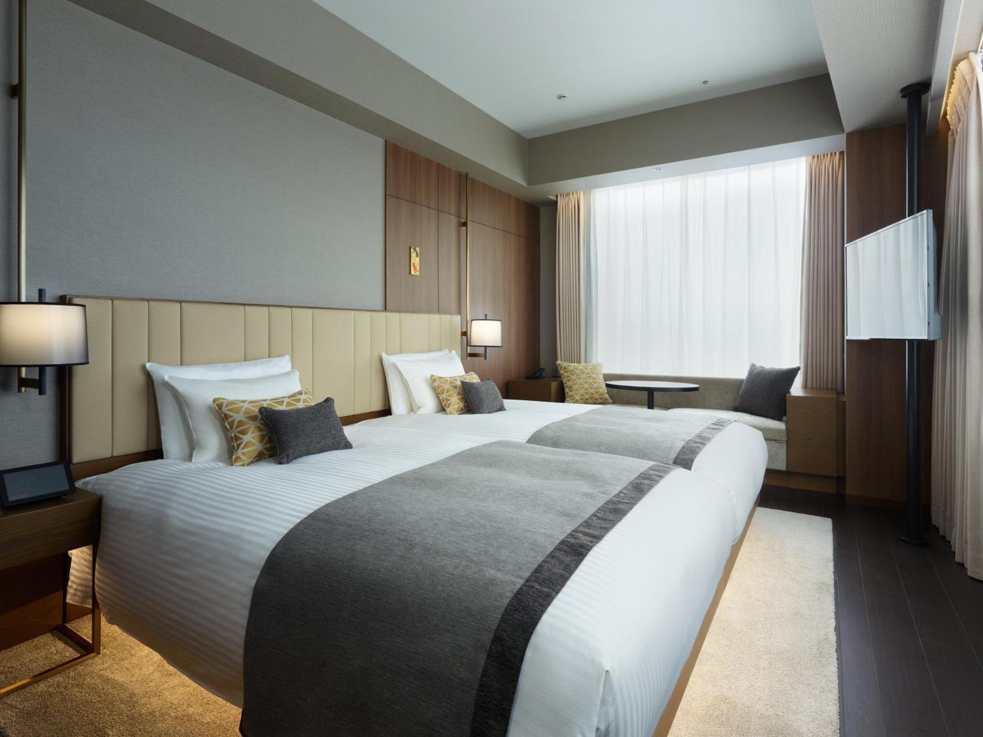 Mitsui Garden Hotel Roppongi Tokyo Premier Zewnętrze zdjęcie The photo shows a modern hotel room featuring two beds with white linens and decorative pillows. The room has a minimalist design, with neutral-colored walls and wooden accents. Natural light comes in through large windows, which are partially covere