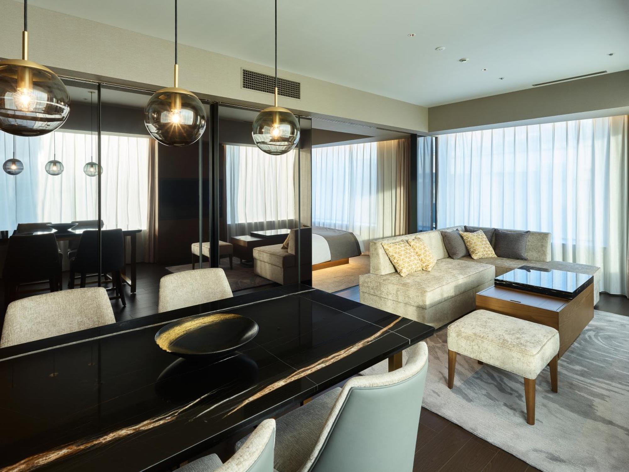 Mitsui Garden Hotel Roppongi Tokyo Premier Zewnętrze zdjęcie The photo shows a modern and stylish living area. It features a dining table with elegant chairs, a comfortable seating area with a light-colored sofa, and a coffee table. The room is well-lit by large windows draped with sheer curtains, allowing nat