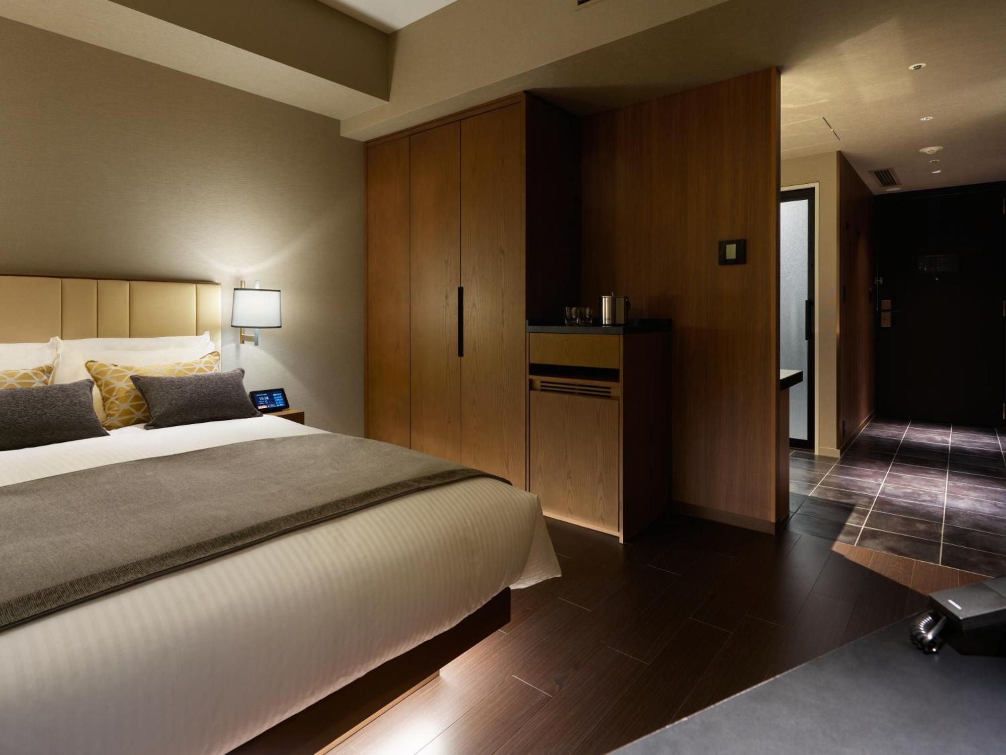 Mitsui Garden Hotel Roppongi Tokyo Premier Zewnętrze zdjęcie The photo shows a modern hotel room featuring a neatly made bed with decorative pillows. The room has wooden accents, including a wardrobe and cabinetry, contributing to a warm ambiance. A bedside lamp is on one side of the bed, and there's a small a
