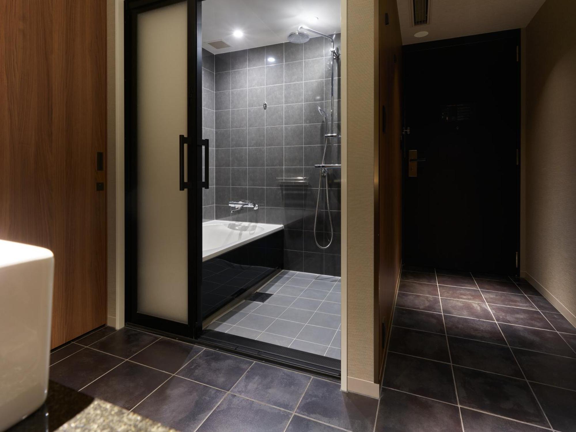 Mitsui Garden Hotel Roppongi Tokyo Premier Zewnętrze zdjęcie The photo shows a modern bathroom area. On the left, there is a white toilet, and in the center, there is a shower area with a glass door. The shower has a modern design, featuring wall tiles in dark gray and a showerhead mounted on the wall. Next to